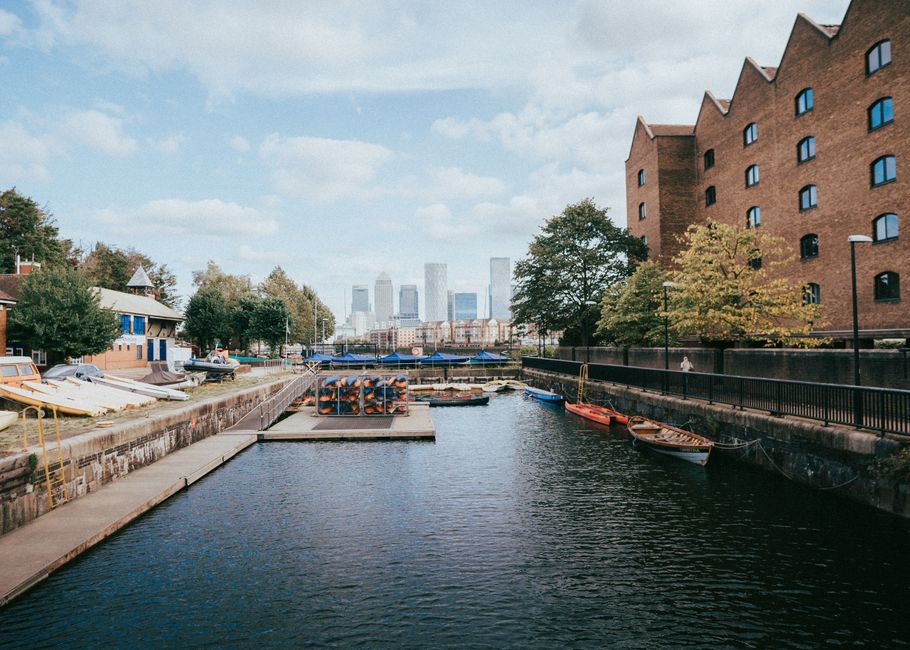 An aerial view of a modern city skyline featuring a cluster of high-rise office buildings and residential towers along a canal or river, with some buildings under construction visible on the lower lef